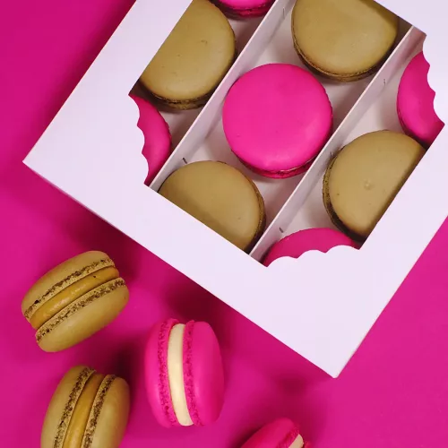 Weiße Sweet Box/Schachtel mit Sichtfenster und neun braunen und pinken Macarons auf pinkem Hintergrund