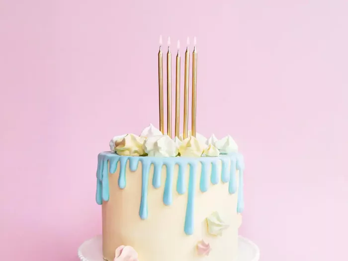 Eine weiße Torte mit hellblauem Zuckerguss Drip und goldenen Kerzen der Marke PartyDeco vor rosa Hintergrund