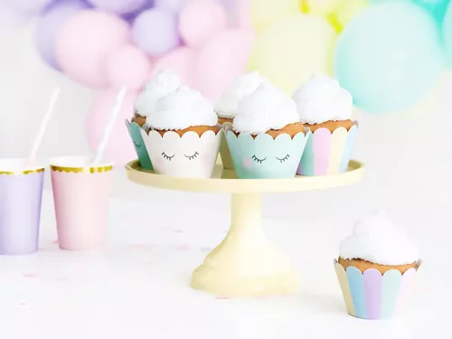 Fünf Einhorn Cupcakes mit pastellfarbenen, gestreiften Muffinförmchen mit Wimpernaufdruck und weißem Frosting auf einer gelben Tortenplatte