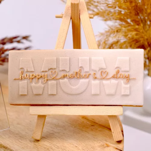 Ein beiger Keks mit gestempeltem "Happy Mother's Day, Mum" Schriftzug auf einer kleinen Staffelei