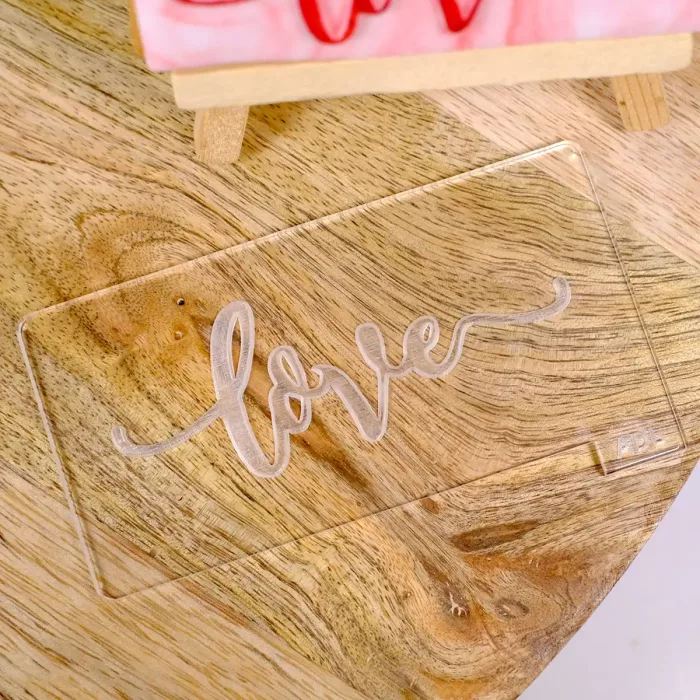 Ein Keksstempel aus transparentem Acrylglas mit der Gravur "love" auf einem Untergrund aus Holz