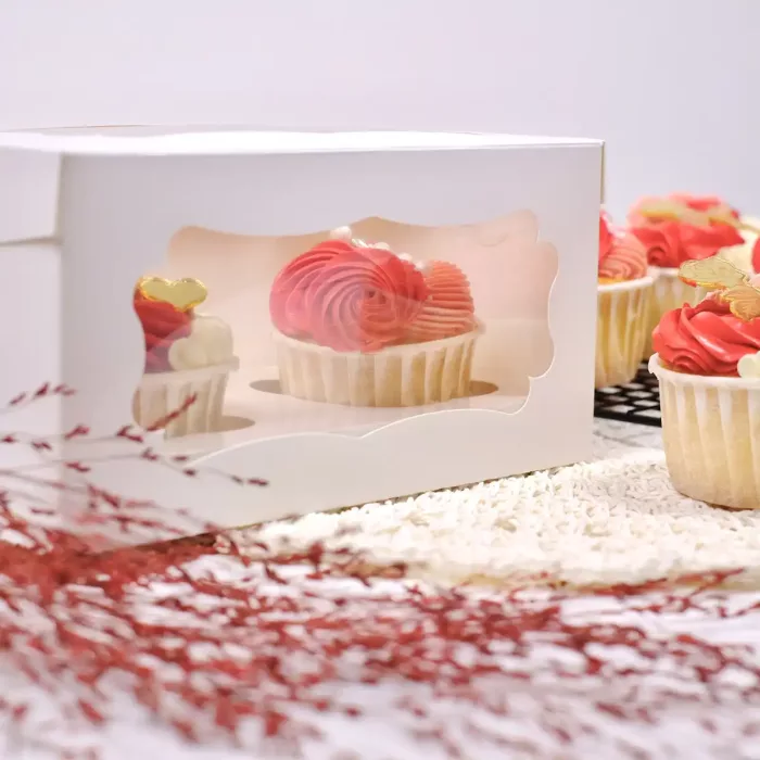 Weiße Cupcake Box für zwei Cupcakes mit transparentem Sichtfenster und zwei Cupcakes mit rosaroter Creme auf dekoriertem Tisch