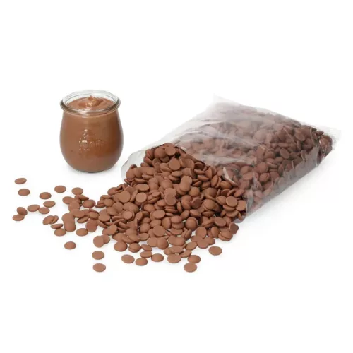 Eine transparente Packung mit Vollmilch Schokoladendrops der Marke Callebaut, teilweise ausgeschüttet, neben einem Glas mit Schokoladenpudding