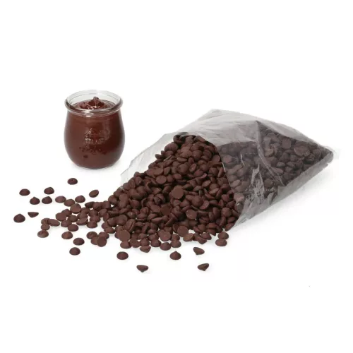 Eine transparente Packung mit dunklen Zartbitter Schokoladendrops der Marke Callebaut, teilweise ausgeschüttet, neben einem Glas mit dunklem Schokoladenpudding