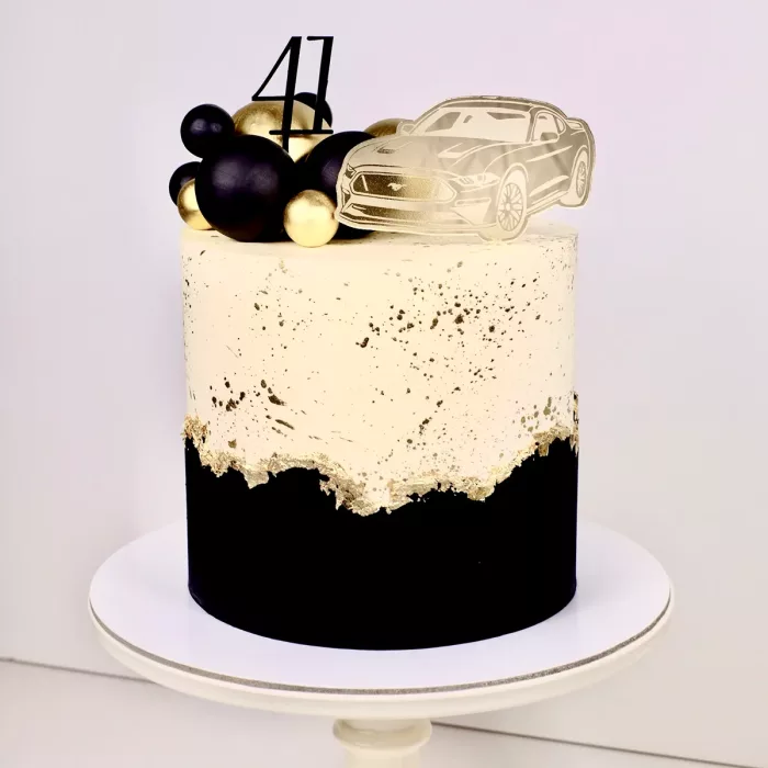 Eine schwarz goldene Torte mit einem Cake Topper in Form eines goldenen Mustangs und einer schwarzen 41 oben drauf.