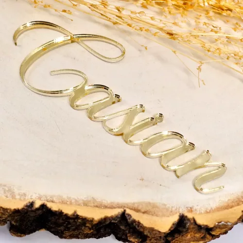 Nahaufnahme eines personalisierten Cake Toppers mit der Aufschrift "Casian" in geschwungener, Schrift aus goldenem Acryl auf einer Holzplatte