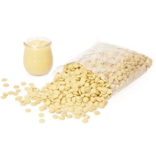 Eine transparente Packung mit weißen Schokoladendrops der Marke Callebaut, teilweise ausgeschüttet, neben einem Glas mit weißem Pudding