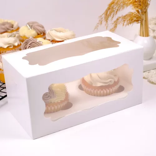 2er Cupcake Box mit zwei Creme farbenen Cupcakes befüllt. Im Hintergrund Trockenblumen in einer Vase und weitere Cupcakes.