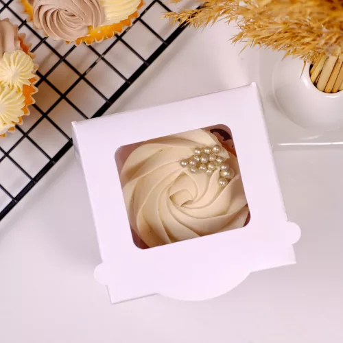 Eine geschlossene weiße Cupcake Box mit Sichtfenster und einem Cupcake mit beiger Buttercremeblume und goldenen Streusel