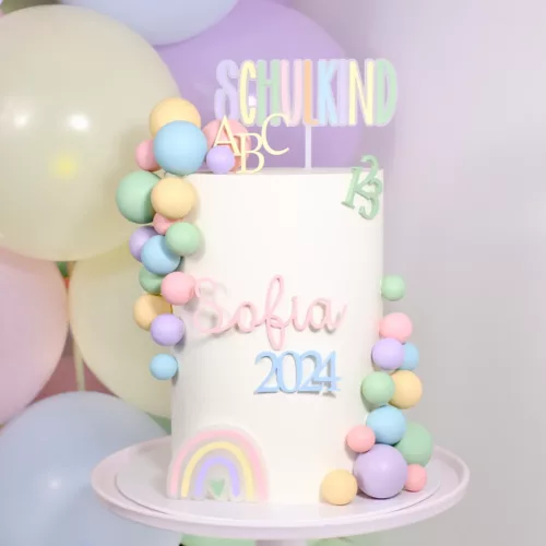 Torte mit Bunten Kugeln und einen Cake Topper mit dem Schriftzug SCHULKIND und Sofia 2024.