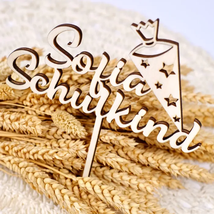 Detailaufnahme eines Cake Topper aus Holz mit der Aufschrift "Sofia Schulkind" auf Trockenblumen und weißem Hintergrund