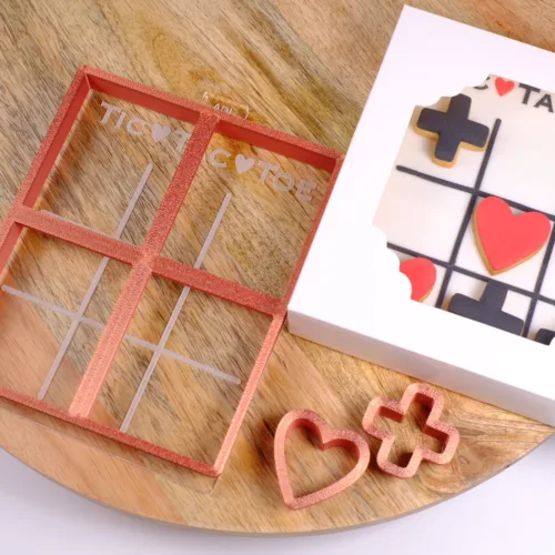 Schwarz weißer Keks mit roten Details in Form eines Tic Tac Toe Spiels. Mit den passenden Ausstecher und dem Keksstempel auf einem Holzbrett.