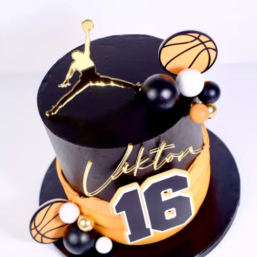 Detailfoto von oben einer Schwarz-Orangen Torte mit goldenem Schriftzug, Basketballer und einer 16 im Vordergrund auf weißem Hintergrund.