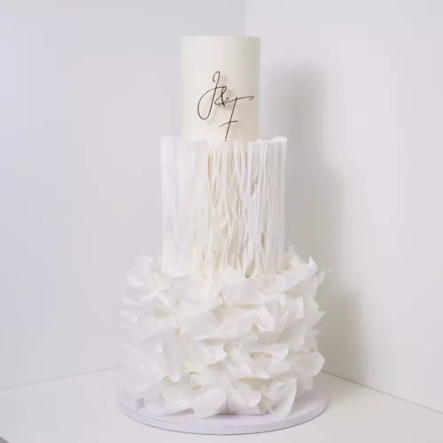 Eleganter Cake Topper aus Acryl Gold mit personalisierten Initialen ‚J & F‘ auf einer modernen, mehrstöckigen Hochzeitstorte in Weiß