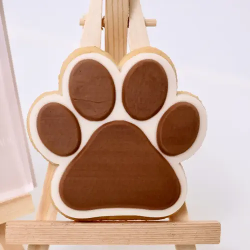 Braun-beiger Keks in Form einer Hundepfote auf einer Staffelei.
