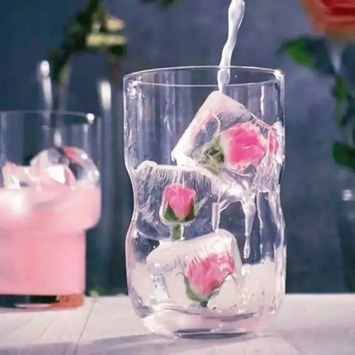 Rosa Damaszener-Rosenknospen in klaren Eiswürfeln im Trinkglas als dekorative Zutat für Cocktails und Getränke.